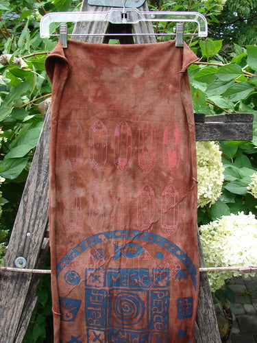Barclay Diagonal Scarf Wrap Belief Spirit Magic Mottled Rust OSFA features purplish-pink surfboard outlines and a blue mandala motif on rust-brown organic cotton, displayed outdoors on a hanger.