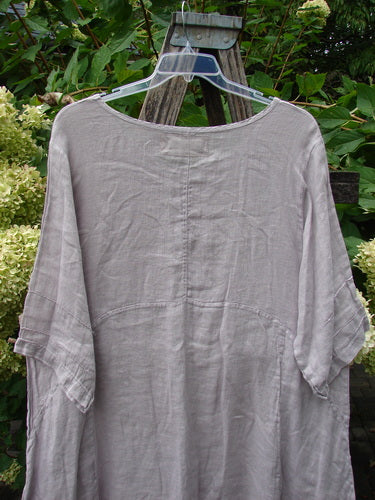Barclay NWT Linen Wave Pocket Dress Floral Bunch Vintage Quartz Size 1, features a loose-fitting tunic with pinched three-quarter sleeves, front drop pockets, and a varying hemline, elegantly draped over a wooden stand.