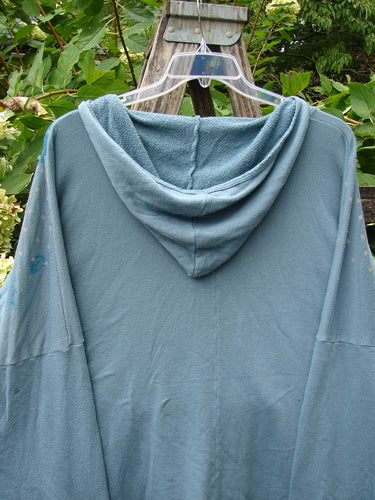 Barclay NWT Fleece Modal Hip To Be Square Hoodie Rain Flower Sea OSFA displayed on a wooden trellis with leafy plants in the background, highlighting its cozy design with a kangaroo pocket and tunnel pocket.