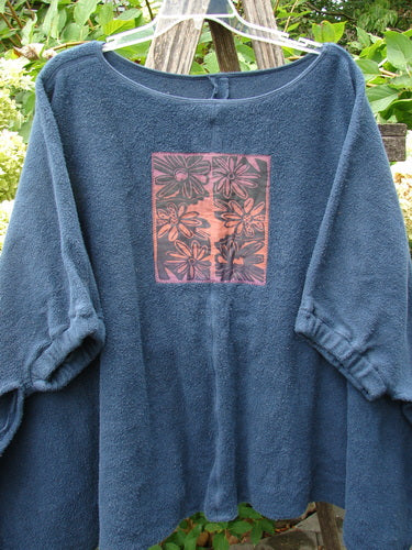 Barclay Celtic Moss Patched Poncho Single Six Daisy Ink Blue OSFA: A cozy navy-blue fleece pullover with daisy floral graphic on the chest, featuring open sides and gathered lower sleeves.