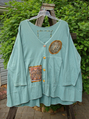 1993 PMU Patched Modernismo Cardigan: A green shirt with a fish on it, adorned with whip-stitched accents and oversized patches.