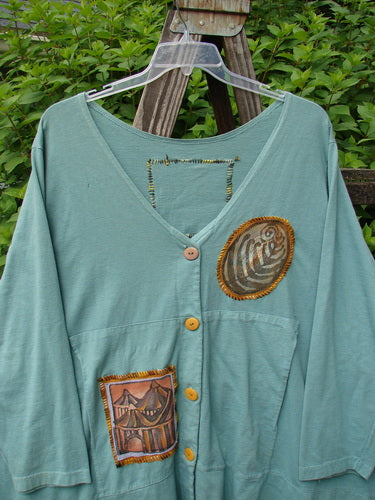 1993 PMU Patched Modernismo Cardigan: Green shirt with a design, fabric patch, buttons, kangaroo pockets, A-line swing, drawcord back, oversized patches, banded hemline.