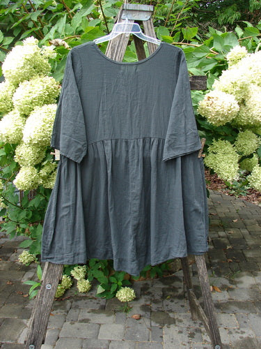 Barclay NWT Textured Terrarium Dress Contour Floral Ironworks Size 1, a loose-fitting slate-gray tunic dress with elbow-length sleeves, displayed on a hanger over a wooden ladder, showcasing its unique silhouette and contour floral design.