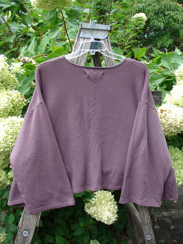 A Barclay NWT Fleece Donna Sweatshirt Frenchtown Logo Fig OSFA, featuring a wide A-line shape, drop shoulders, and a rounded neckline, displayed on a wooden ladder amidst greenery.