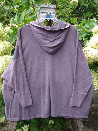 Barclay NWT Cotton Hemp Folklore Hoodie Morning Dove Aura OSFA on hanger, showcasing its cozy fleece texture, hood, kangaroo pockets, and distinctive morning dove theme. Displayed outdoors against a leafy backdrop.