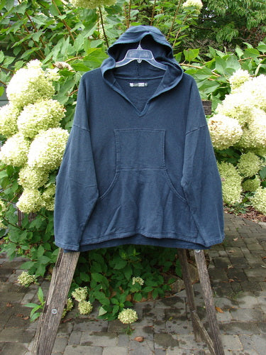 Barclay Cotton Hemp Hip To Be Square Hoodie Rear Botanicals Black OSFA, featuring a kangaroo front pocket, hangs on a hanger, showcasing its cozy fleece texture and hood design against white hydrangeas.