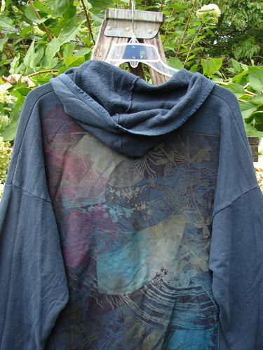 Barclay Cotton Hemp Hip To Be Square Hoodie Rear Botanicals Black OSFA, showcasing a subtle abstract print in blues, purples, and greys across the back panel, hangs outdoors, highlighting its cozy fleece texture.