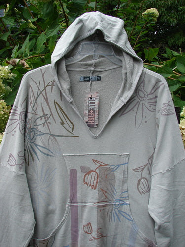 Barclay NWT Fleece Modal Hip To Be Square Hoodie Contour Floral Cloud OSFA: Lightweight gray pullover with v-neckline, stylized floral pattern, kangaroo pocket, and attached tag, displayed outdoors.