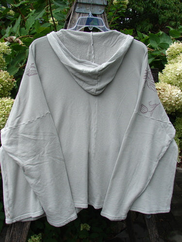 Barclay NWT Fleece Modal Hip To Be Square Hoodie Contour Floral Cloud OSFA features a light-gray, hooded pullover with wide sleeves, displayed stylishly on a wooden ladder amidst lush foliage.