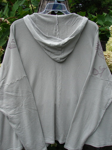 Barclay NWT Fleece Modal Hip To Be Square Hoodie Contour Floral Cloud OSFA, featuring a loose-fit design with hood, displayed on a hanger amid green foliage.