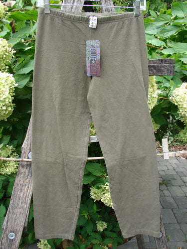 Barclay NWT Cotton Lycra Crop Legging Unpainted Brown Earth Size 0, lightweight with elastic waistband, hangs clipped to a wooden frame, showcasing its full length amid a backdrop of greenery.
