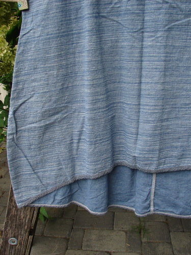 Barclay NWT Light Weight Chambray Shift Stripe Denim Light Size 0 drapes elegantly over a wooden bench, showcasing its striped linen fabric and flowing silhouette amidst a serene garden setting.