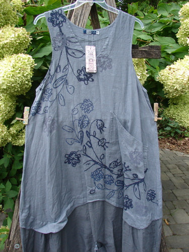 Barclay NWT Linen Explorer Jumper Trailing Botanicals Blue River Mist Size 0 features a grey, sleeveless tunic with asymmetrical hem, floral motifs, scoop neckline, and large patch pocket, hanging on a clear hanger.