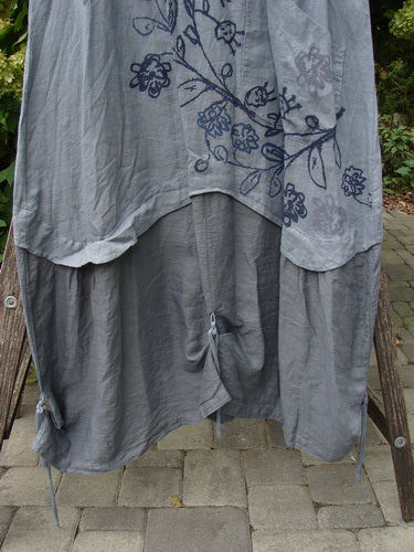 Barclay NWT Linen Explorer Jumper in Blue River Mist, featuring a two-layered, loose fit with floral vine print, drawstring tie, and side bows, hangs over a wooden chair outdoors.
