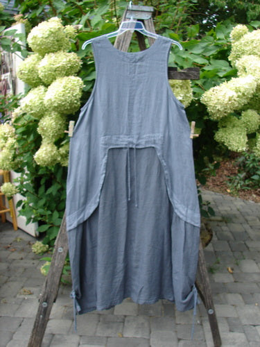 Barclay NWT Linen Explorer Jumper in Blue River Mist, a sleeveless smock-style dress featuring a scoop neckline, overlay bodice, and generous upper pocket, hangs outdoors, showcasing its unique trailing botanicals theme.