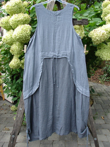 Barclay NWT Linen Explorer Jumper Trailing Botanicals Blue River Mist Size 0 displayed on a hanger, showcasing its sleeveless, apron-style design with oversized side openings and tie-back waist, hanging on an outdoor ladder.