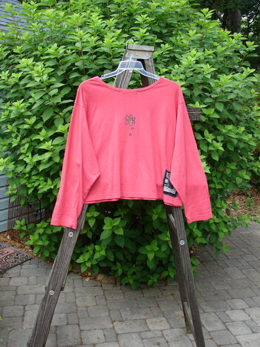 1997 Long Sleeved Crop Tee Tri Window Box Geranium Size 2: A pink shirt on a wooden ladder, featuring a wide crop shape, vented sides, drop shoulders, and a tri window box theme paint.