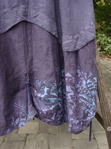 Barclay NWT Linen Explorer Jumper Botanical Blossom Purple River Mist Size 0, featuring a scoop neckline, offset pocket, and blue floral motifs near the hem, draped on a rustic bench outdoors.