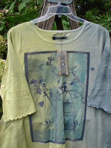 Barclay NWT Three Quarter Sleeved Cafe Tee in Free Bird Mottled Violet Citron, featuring a stylized bird-and-birdcage motif, hangs outdoors showcasing its unique A-line shape and sweet curly edgings.