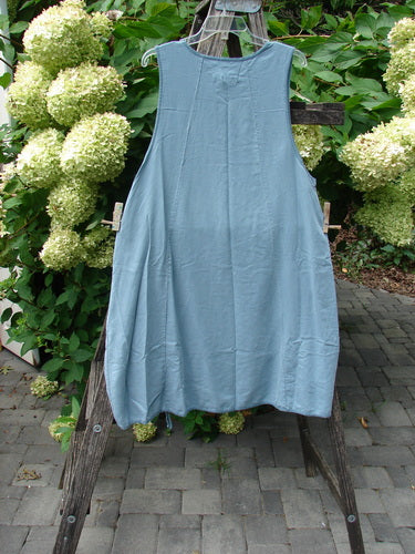 Barclay NWT Lyocell Joyous Jumper Unpainted Sea Green Size 0 displayed on a wooden trellis, showcasing its loose-fitting, sleeveless design with deep arm openings and double drop front pockets.