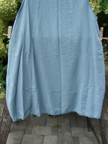Barclay NWT Lyocell Joyous Jumper Unpainted Sea Green Size 0 draped over a wooden frame outdoors, showcasing its sweeping A-line shape, deep arm openings, and double drop front pockets.