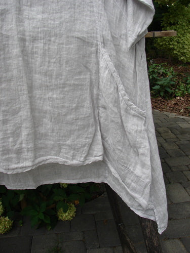Barclay NWT Linen Zen Pocket Tunic Unpainted Dove Size 0 displayed on a wooden stand; features three-quarter sleeves, A-line shape, oval neckline, dual pockets, and varying hemline, set against a patio backdrop.