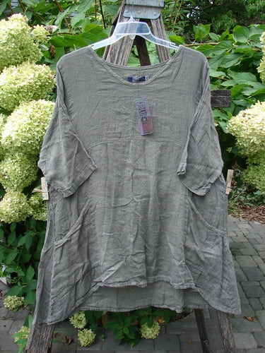 Barclay NWT Linen Zen Pocket Tunic Unpainted Stone Beach Size 0: A loose-fitting, mid-length tunic with a round neckline, elbow-length sleeves, front patch pockets, and a subtle horizontal bust seam, hanging outdoors.
