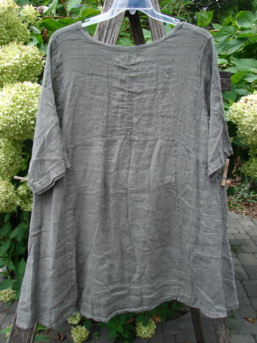 Barclay NWT Linen Zen Pocket Tunic in muted gray-green, featuring a wide neckline, elbow-length sleeves, A-line shape, with dual drop pockets and visible seam lines. Hangs outdoors on a clear hanger.