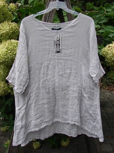 Barclay NWT Linen Zen Pocket Tunic Unpainted Pearl Smoke Size 0, features a lightweight linen with a curved hem, dropped sleeves, front pockets, and a rounded neckline, displayed on a hanger outdoors.