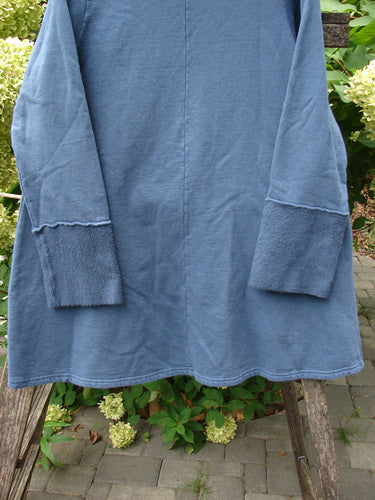Barclay NWT Fleece Cowl Neck Sweatshirt Metallic Daisy Vintage Indigo Size 0 hanging on a wooden trellis, showcasing its long sleeves, textured cuffs, and A-line shape amidst a serene outdoor setting.