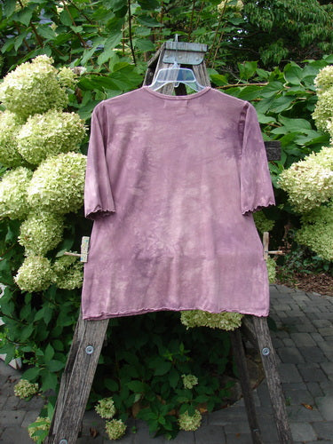 Barclay NWT Cotton Lycra Horizon Tee BF Logo Cats Mottled Pinkberry Size 0 displayed on a wire hanger over a wooden stepladder, highlighting its unique curved edges and retro cat-themed design against lush greenery.