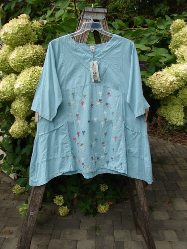 Barclay NWT Batiste Cross Over Urchin Pocket Tunic Tiny Tulip Turquoise Size 0 displayed outdoors, featuring elbow-length sleeves, two front pockets, colorful embroidered flowers, and a tag at the neckline.