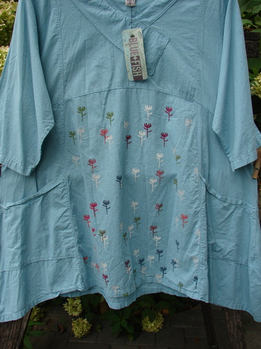 Barclay NWT Batiste Cross Over Urchin Pocket Tunic features a loose fit, V-neck, elbow-length sleeves, and floral embroidery. Displayed outdoors, highlighting its airy fabric and artistic design.