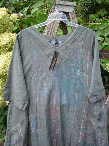 Barclay NWT Linen Cross Over Urchin Pocket Dress Vertical Rain Smudge Stick Size 0 draped on a hanger, showcasing its patch pockets, elbow-length sleeves, and a cross-over V-neckline with a subtle paint-splatter effect.