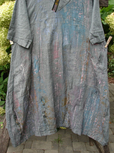 Barclay NWT Linen Cross Over Urchin Pocket Dress in 'Vertical Rain Smudge Stick' hangs outdoors, showcasing its artistic pastel paint splatters, crossover V-neck, and unique drop flop pockets.
