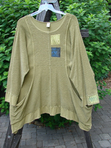 Barclay Patched Crepe Perennial Tunic Top Woods Olive Size 2: A green shirt with a patch on a rack, made from thick textured cotton crepe. Features include front drop wrap side pockets, an empire waist seam, and banded lower sleeves and hemline.