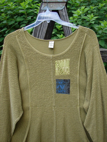 A Barclay Patched Crepe Perennial Tunic Top in Olive, size 2. A green sweater with patchwork designs, textured fabric, and banded sleeves.