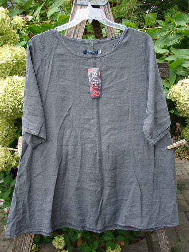 Barclay NWT Linen Lucida Top Unpainted Diatom Size 0 on a hanger, showcasing its flowy A-line shape, rounded neckline, and almost three-quarter sleeves, set against lush foliage.