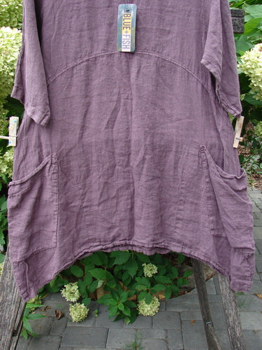 Barclay NWT Linen Urchin Pocket Tunic Unpainted Fig Size 0, featuring elbow-length sleeves, two front patch pockets, and a rounded neckline, displayed outdoors against green foliage and hydrangeas.