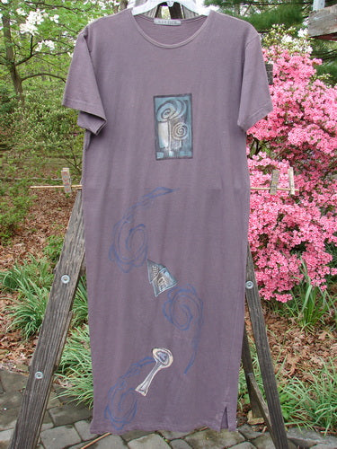 1996 Long Tee Dress Lolly Flower Violet Field Altered Size 0 featuring a rounded neck, seamless front and back, short wide sleeves, and a pegged vented hemline, displayed on a hanger against a plain backdrop.