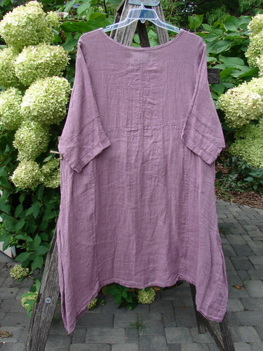 Barclay NWT Linen Wave Pocket Dress in Dried Floral Tulsi Rose, displayed on a wooden ladder, features a rounded neckline, seamless bodice, drop pockets, pinched sleeves, and varying hemline.