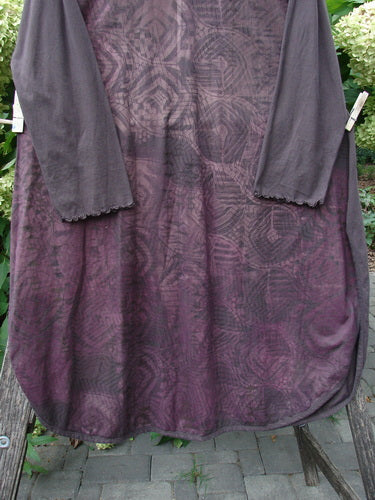 Barclay NWT Natalia Tunic Grid Pod Red Peat Size 0, featuring muted purple body with geometric patterns, gray long sleeves, and lettuce edges, hanging on a clothesline with a rounded neckline and hemline.