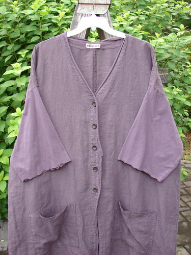 Barclay Linen Cotton Sleeve Pocket Cardigan Unpainted Dusty Plum Size 2: A purple shirt with pockets on a fence, made from medium weight linen with organic cotton accents. Features include wooden buttons, drop shoulders, and a V-shaped neckline.
