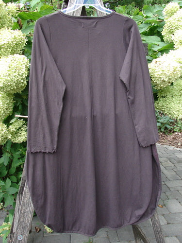 Barclay NWT Natalia Tunic Grid Pod Red Peat Size 0 features a long, loose fit with a round neckline, curved hem, and long sleeves with lettuce edges, hanging against a floral backdrop.