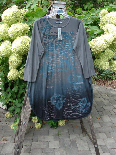 Barclay NWT Natalia Tunic Rain Pod Twilight Grey Size 0, a slate gray tunic with a charcoal hem, dot and floral motifs, hangs from a ladder, showcasing its rounded neckline and lettuce-edged sleeves.