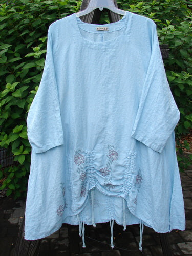 Barclay Linen Venetian Square Neck High Vent Tunic Dress in Daisy Chain Water. A flowing blue dress on a clothes rack. Feminine hourglass shape, wider hip and hemline, S-shaped seams, softly rolled neckline, A-line shape, high vented sides, triple draw cords. Size 2.