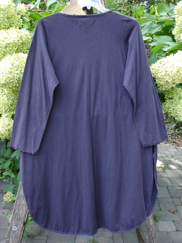 The Barclay NWT Natalia Tunic in Dried Floral Metallics, Plum River Size 1, features a rounded neckline, lettuce-edged long sleeves, and high side vents, displayed against a garden setting.