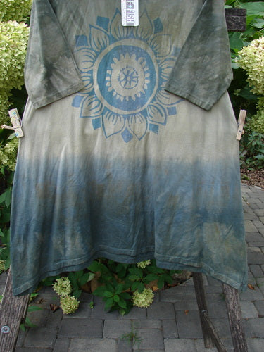 Barclay NWT Wander Tunic Tee Sunflower Mottled Vintage Camo Size 0: Loose-fitting tunic with olive to slate-blue gradient, mandala graphic, and long sleeves, displayed outdoors against hydrangeas, suggesting artistic individuality.
