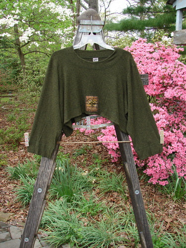 2000 Patched Rayon Lycra Rib Overtop Green Oak Heather Size 1, displayed on a wooden ladder, showcasing its unique upward scooping hemline and exterior stitchery, perfect for layered looks.