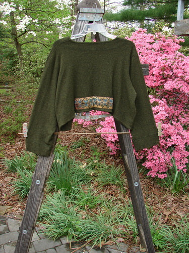 2000 Patched Rayon Lycra Rib Overtop Green Oak Heather Size 1 displayed draped on a wooden ladder, showcasing its unique texture, exterior stitchery, and painted Celtic-themed patches.